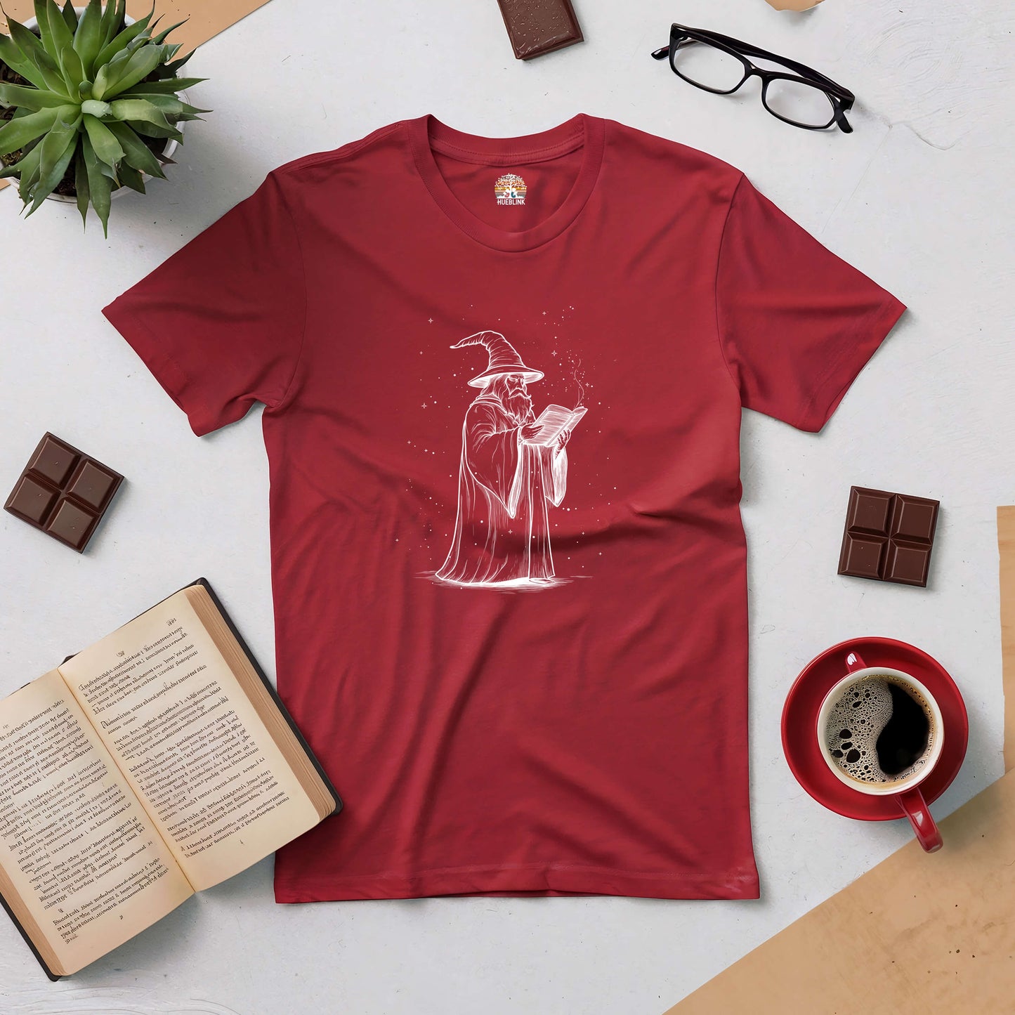 Red t-shirt featuring a mystical wizard engrossed in a grimoire, surrounded by books and coffee, perfect for fantasy lovers.