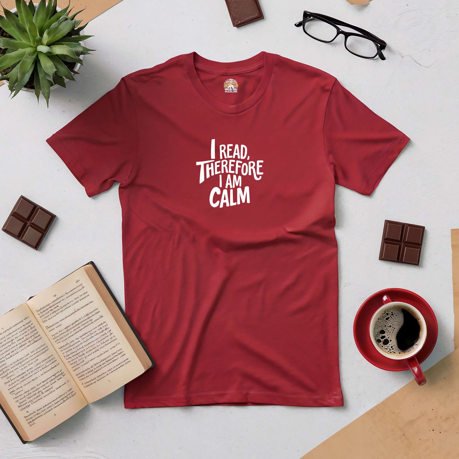 Red "I Read, Therefore I Am Calm" t-shirt for serene readers, displayed with books, glasses, chocolate, coffee, and a plant.