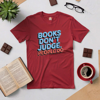 Red tee with "Books Don't Judge, People Do" text, surrounded by books, glasses, and coffee, perfect for book lovers.