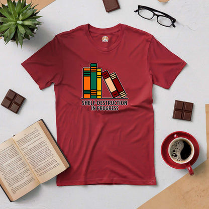 Red "Shelf-Destruction in Progress" tee with colorful books graphic, surrounded by coffee, chocolate, and an open book.