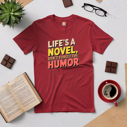 Red tee with "Life's a Novel, Don't Forget the Humor" text, surrounded by books, coffee, plant, glasses, and chocolate.