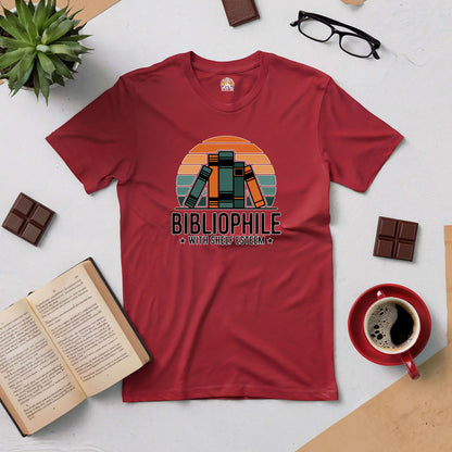 Red "Bibliophile with Shelf Esteem" tee, showcasing a retro book design, surrounded by books, chocolate, and coffee.