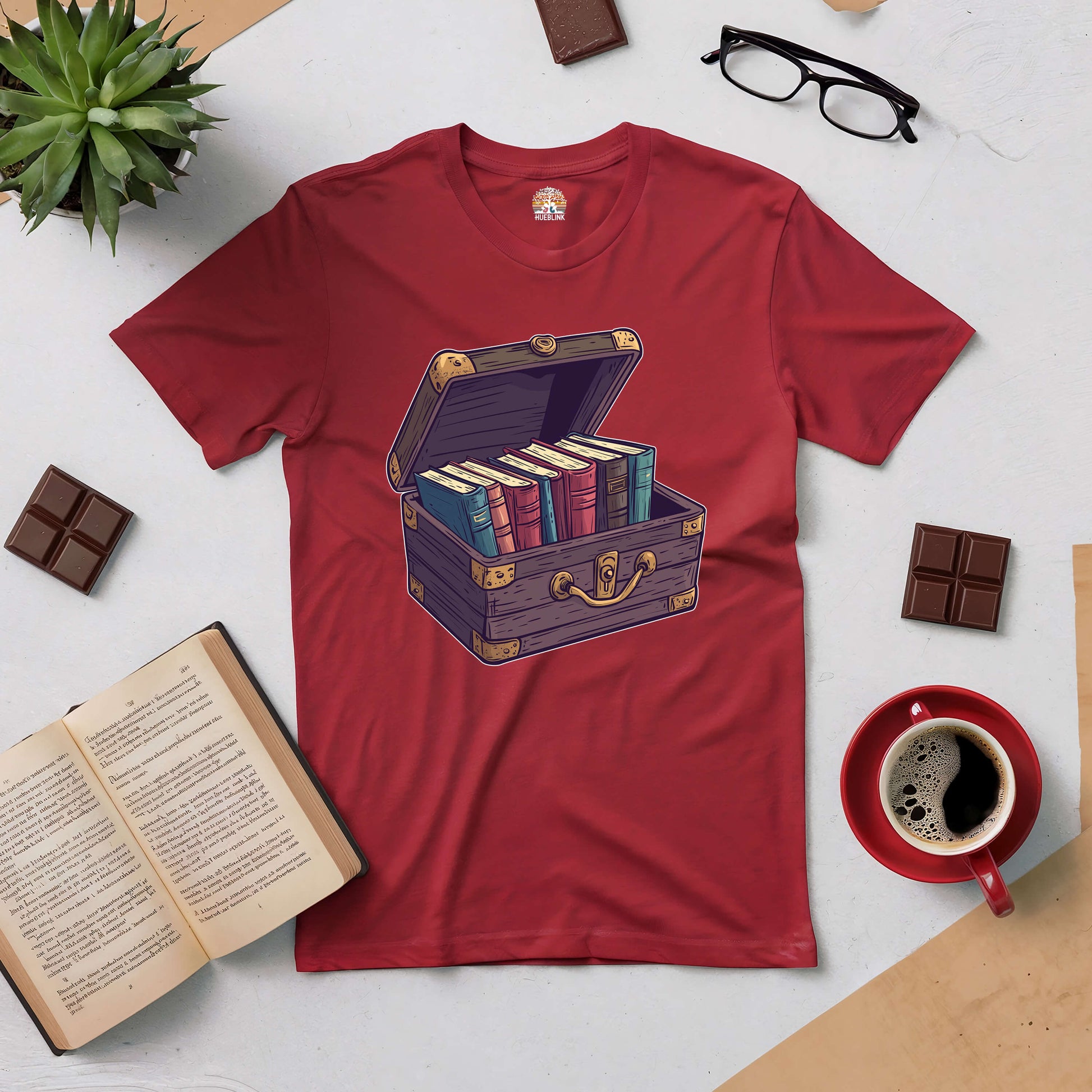 Red Priceless Treasure Tee featuring a chest filled with books, surrounded by coffee, chocolate, and an open novel.