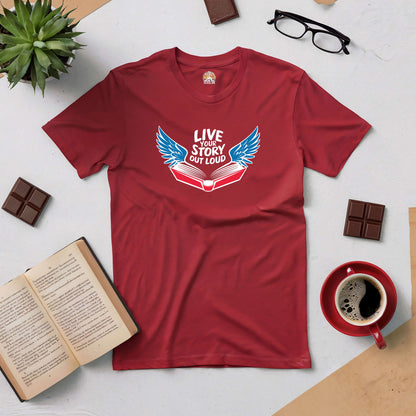 Red "Live Your Story Out Loud" t-shirt with winged book design, surrounded by coffee, open book, glasses, and chocolate.