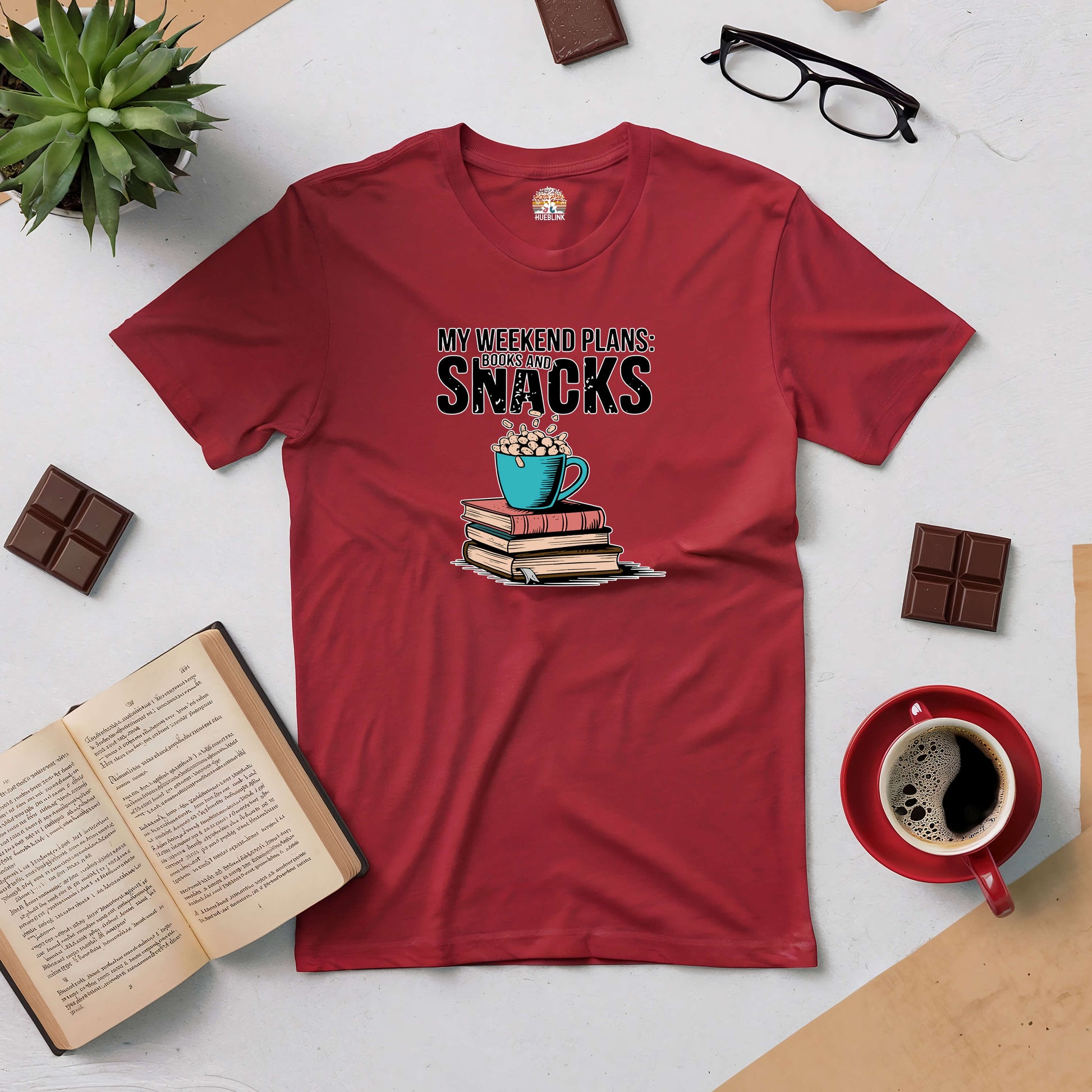 Red tee with "My Weekend Plans: Books & Snacks" design, surrounded by books, chocolate, coffee, and glasses on a cozy setup.