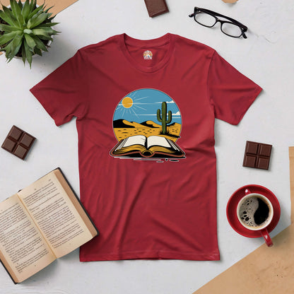 Silent Desert Tee with desert landscape and open book design, surrounded by coffee, chocolate, and reading glasses on a table.