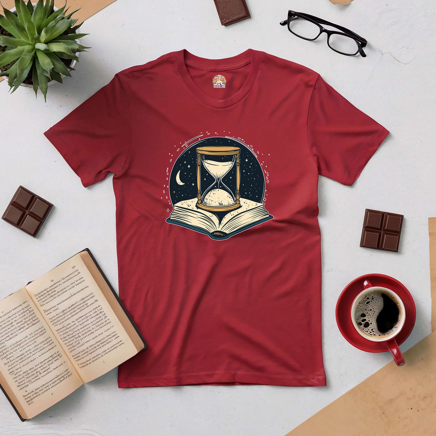 Red "Chronicles of Time and Space" tee featuring hourglass and open book design, surrounded by coffee and reading items.