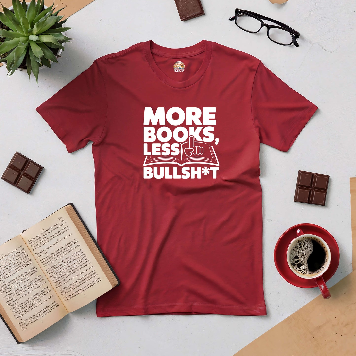 Red tee with "More Books, Less Bullsh*t" text, surrounded by coffee, glasses, open book, and chocolate. Perfect for book lovers.