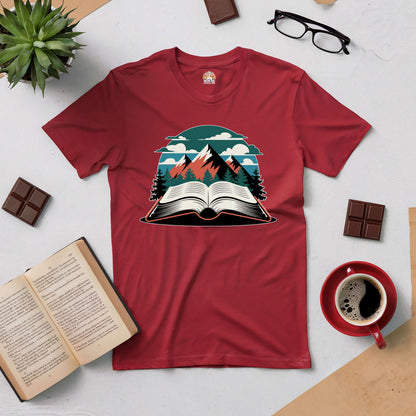 "Summits of Inspiration Tee with book and mountain design surrounded by coffee, books, and chocolate on a flat lay desk setup"