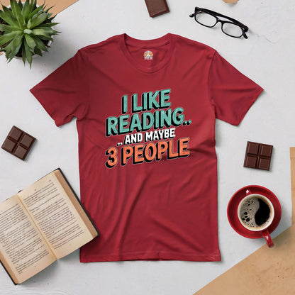 Red tee with "I Like Reading... And Maybe 3 People" text, surrounded by books, coffee, chocolate, and glasses – perfect for book lovers.