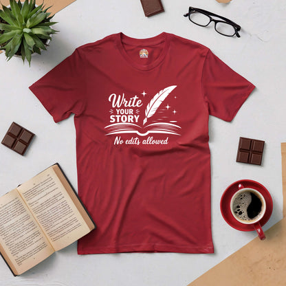 Red "Write Your Story, No Edits Allowed" tee with feather graphic, surrounded by book, chocolate, coffee, glasses, and plant.