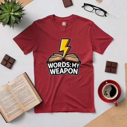 Red "Words: My Weapon" tee with a lightning bolt over an open book, symbolizing the power of language, surrounded by books and coffee.