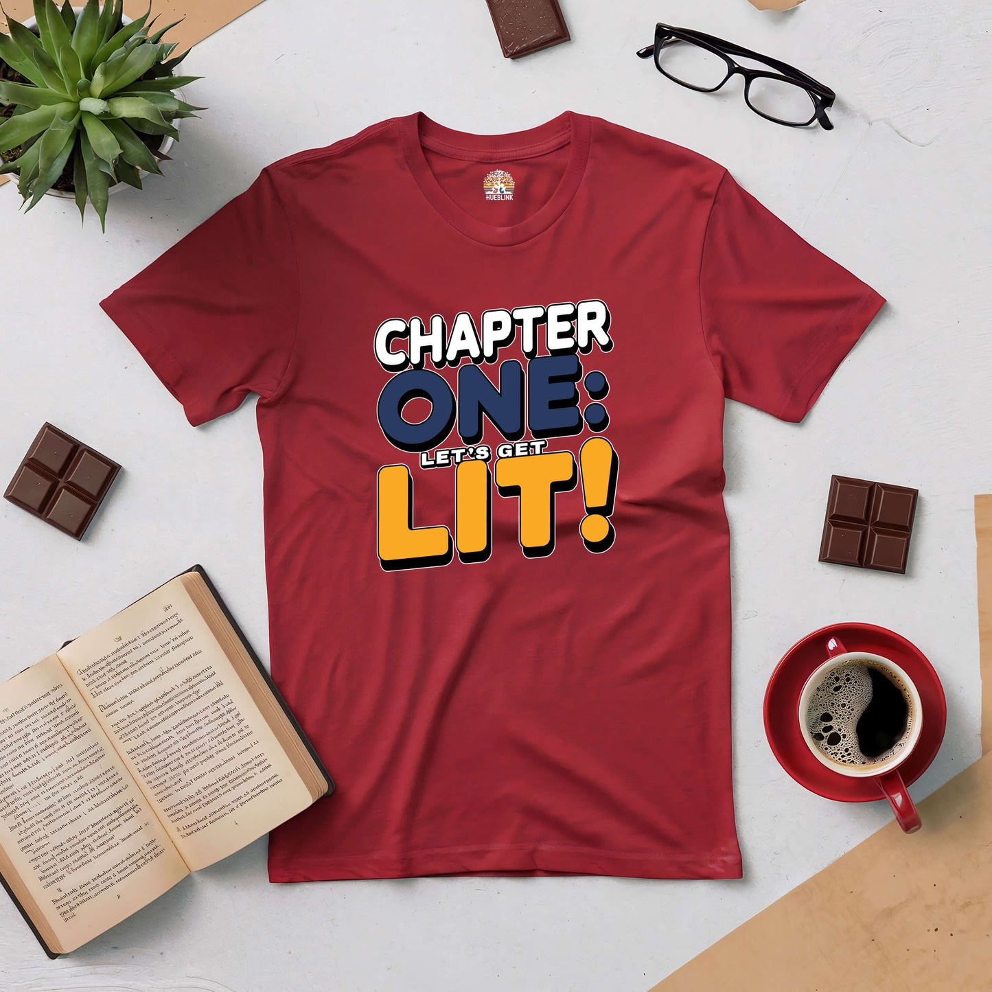 Red "Chapter One: Let's Get Lit!" tee surrounded by books, coffee, and chocolate, ideal for fun-loving book enthusiasts.