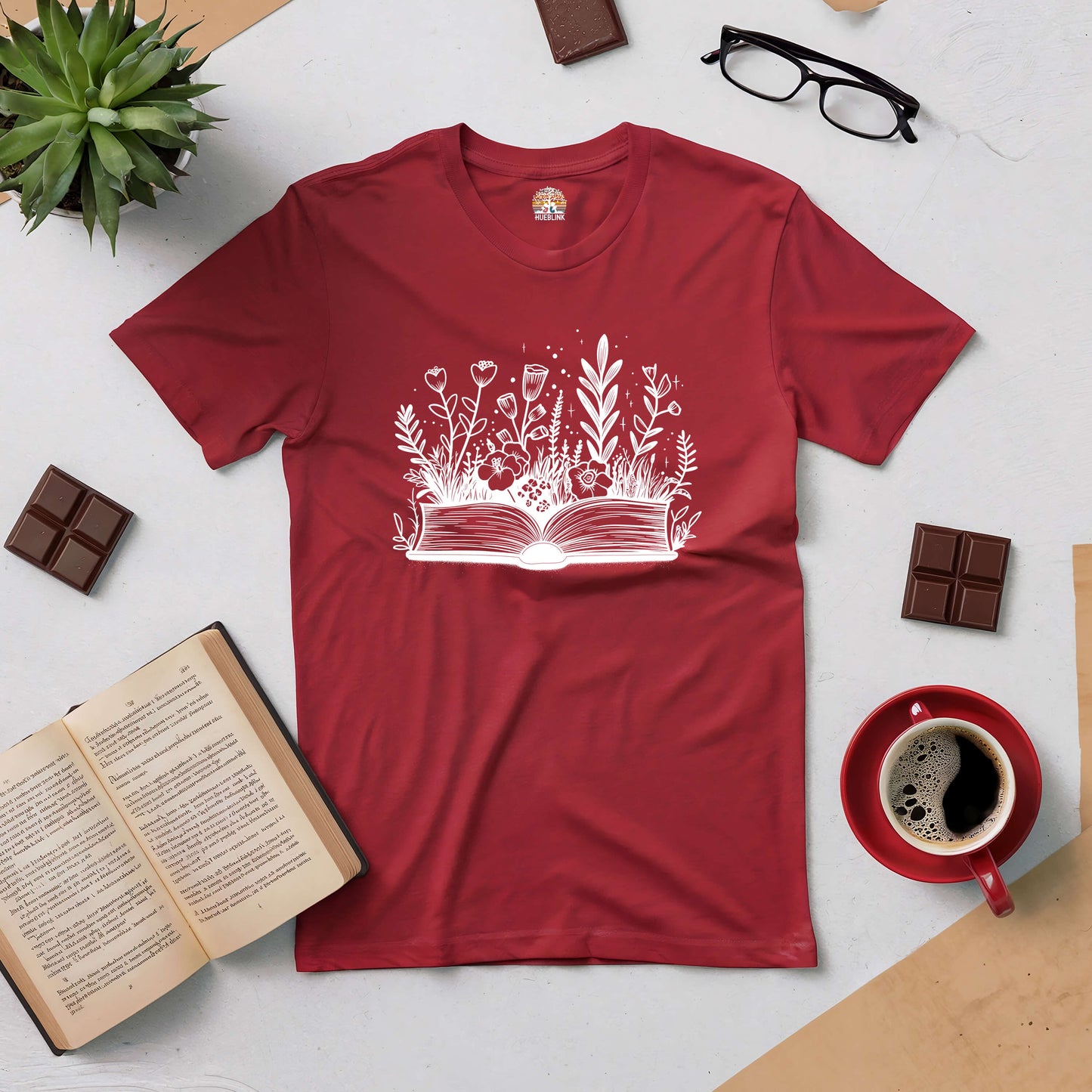 Red Books and Blooms tee with floral book design, surrounded by coffee, chocolate, glasses, and an open book.