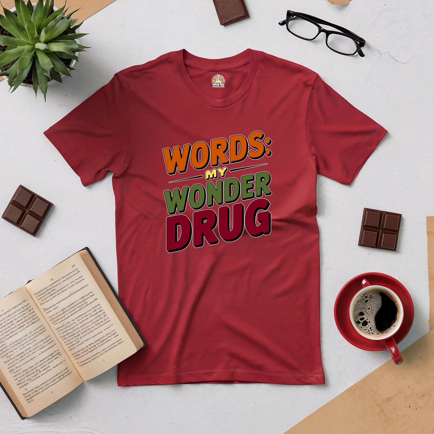 Red Word Therapy tee with "Words: My Wonder Drug" text, surrounded by books, coffee, glasses, and chocolate on a table.