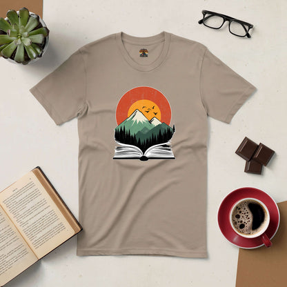 Nature-inspired t-shirt featuring an open book with mountains and sunset, surrounded by coffee, glasses, and a book.