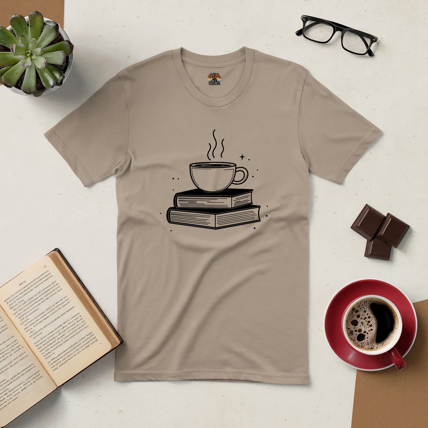 "Brewed for Books Tee featuring coffee cup and book design, surrounded by open book, coffee cup, and glasses on a cozy surface"