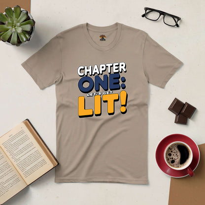 Beige "Chapter One: Let's Get Lit!" tee shirt for book lovers, surrounded by a coffee cup, glasses, chocolate, and an open book.