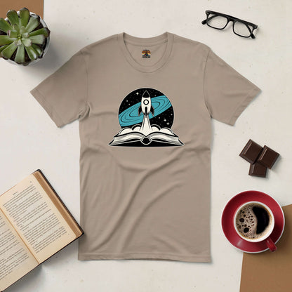 Beige tee with rocket and book design, surrounded by coffee, chocolate, glasses, and succulent. "It's Not Rocket Science" theme.