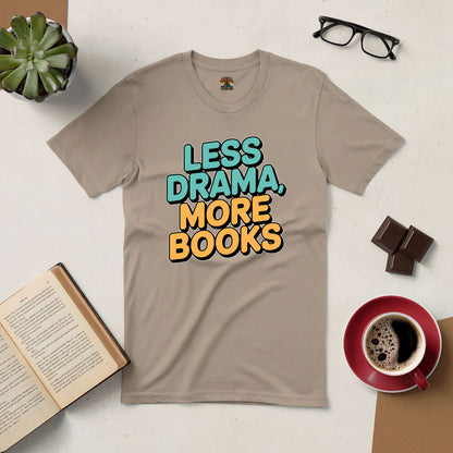 Beige "Less Drama, More Books" tee shirt with open book, glasses, chocolate, coffee, and succulent on a white surface.