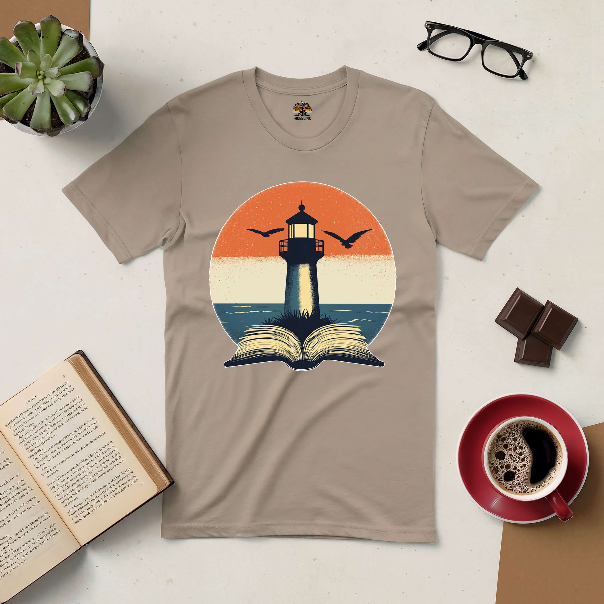 "The Guide I Need Tee with lighthouse and open book design inspiring exploration and wisdom, surrounded by reading and coffee elements."