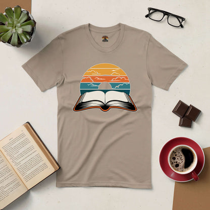 Beige t-shirt with "Narratives in Color" design featuring an open book under a colorful sky, surrounded by coffee and reading materials.