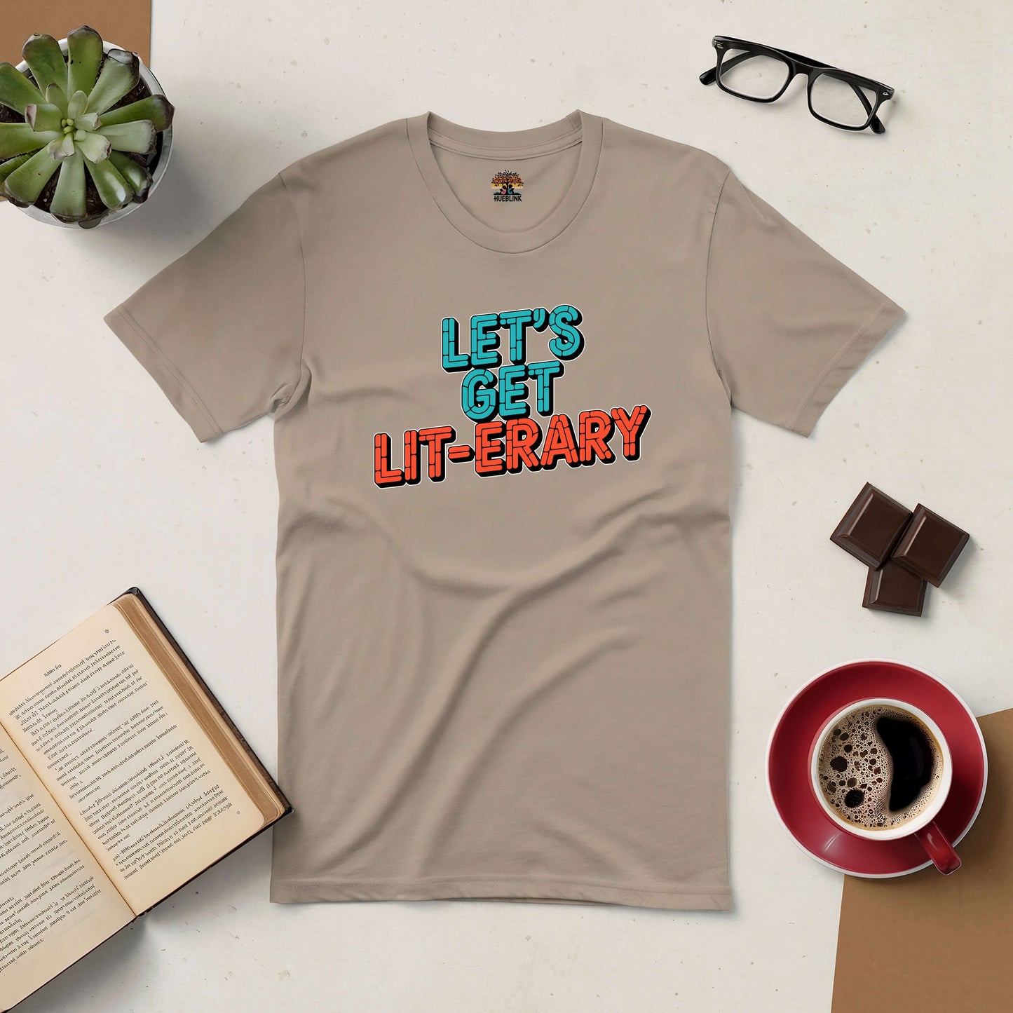 Beige "Let's Get Lit-erary" tee with coffee, books, glasses, and chocolate, perfect for lively book lovers.