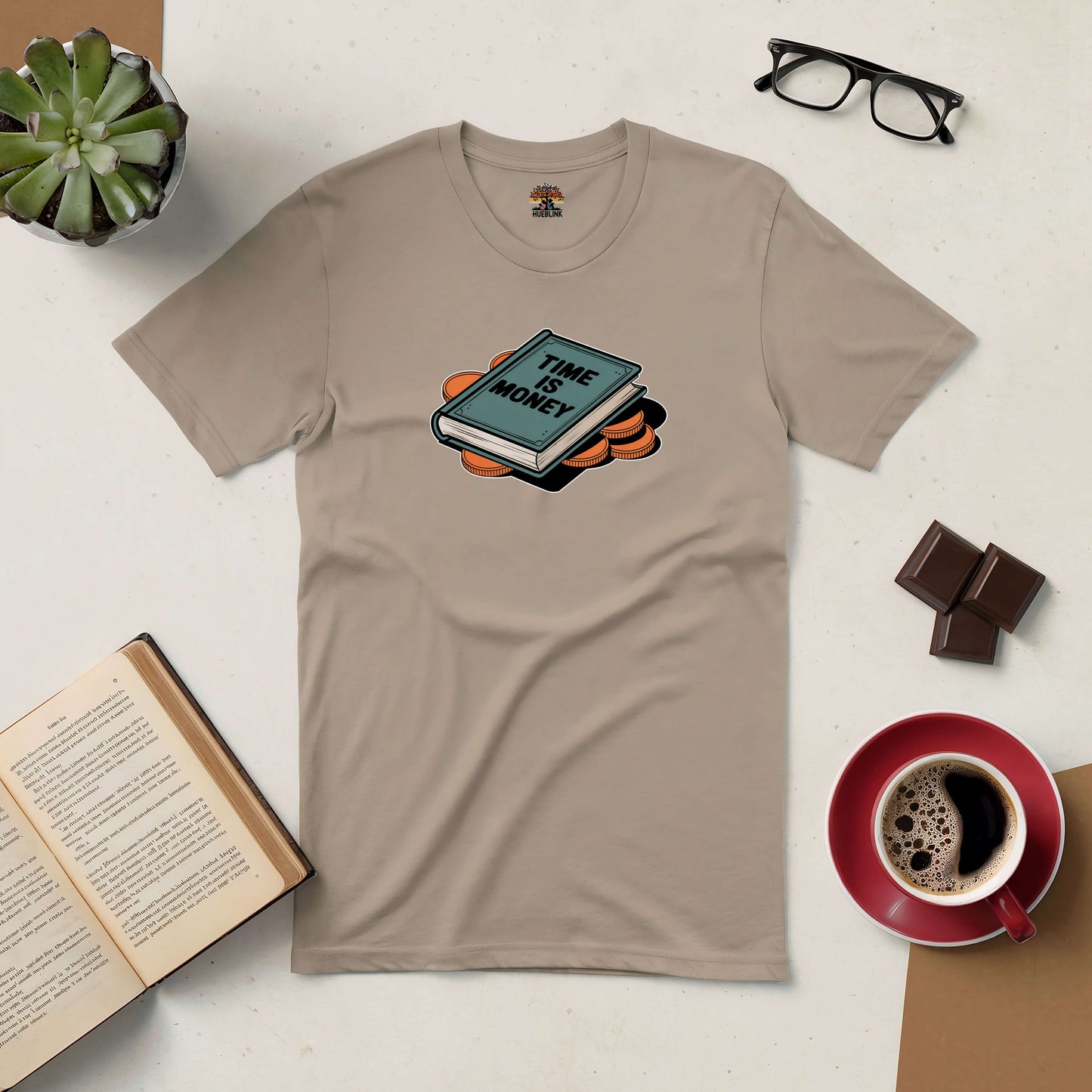 Beige "Time is Money" tee shirt with book and coins graphic, surrounded by reading materials, coffee, and glasses.