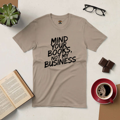 Beige "Mind Your Books, Not My Business" t-shirt for readers, styled with open book, coffee, and glasses on a table.