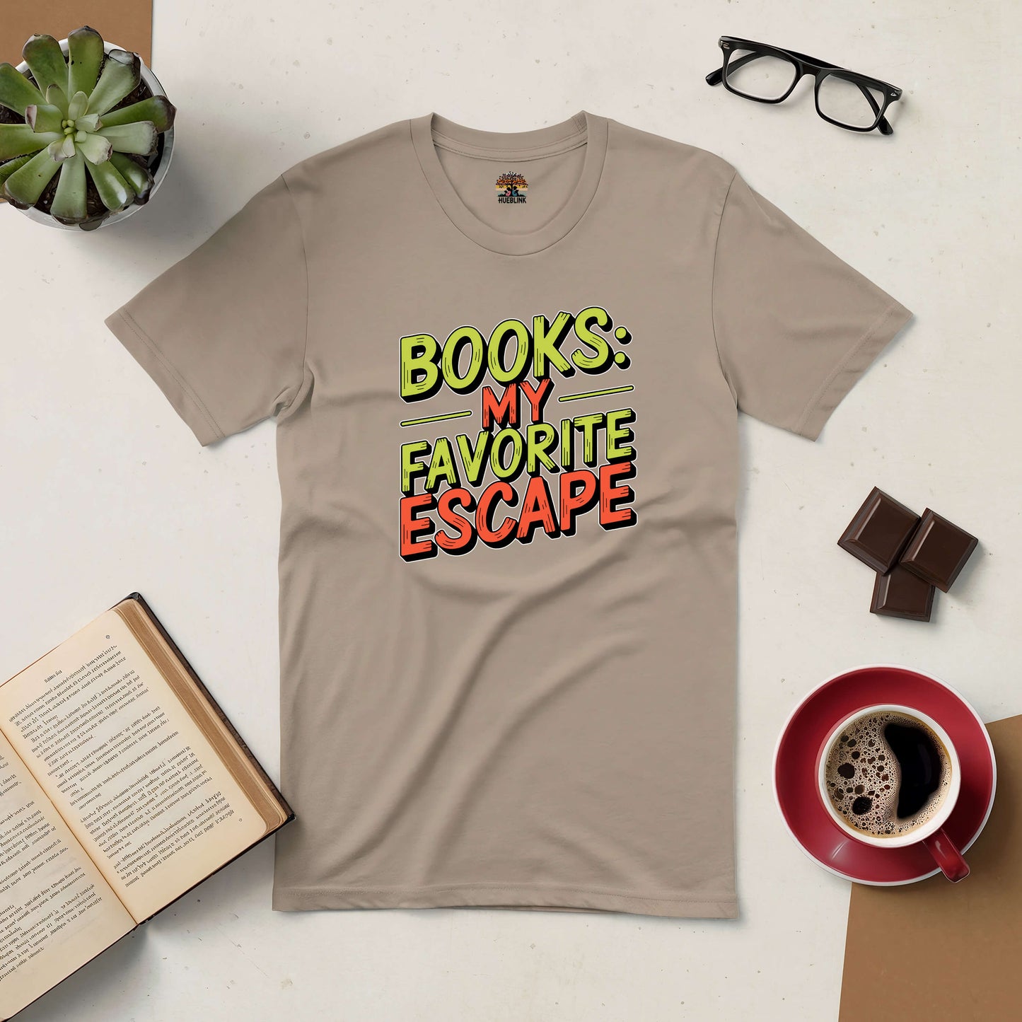 Beige tee with "Books: My Favorite Escape" text design, surrounded by an open book, coffee, glasses, chocolate, and a plant.