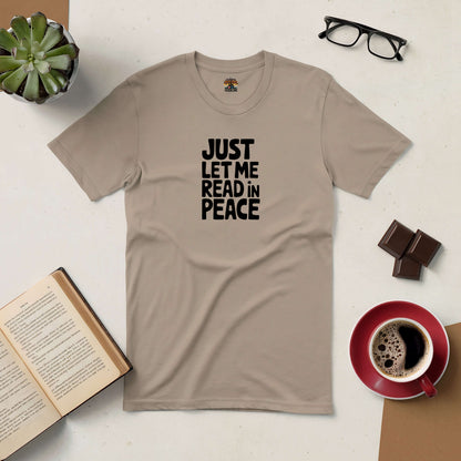 Beige "Just Let Me Read in Peace" tee on table with open book, glasses, coffee, chocolate, and potted plant. Perfect for book lovers.