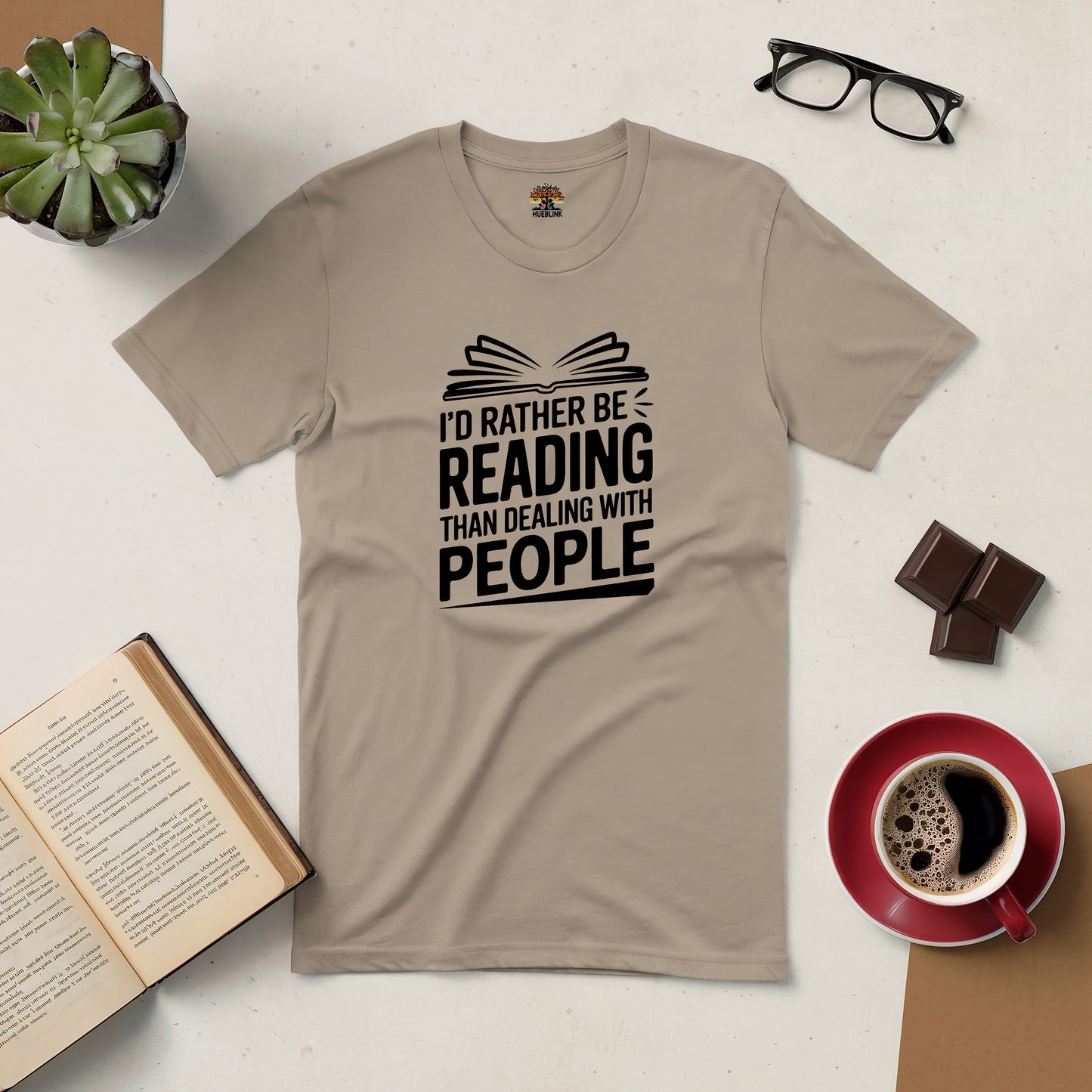 Beige tee with "I'd rather be reading than dealing with people" text, surrounded by books, glasses, coffee, and a plant.