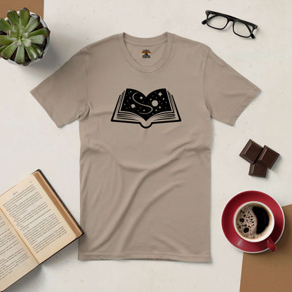 Beige T-shirt with open book and starry design, surrounded by books, coffee, glasses, and chocolate on a table.