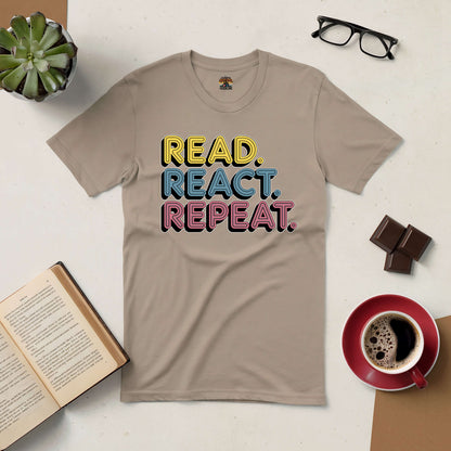 Beige "Read. React. Repeat." tee surrounded by coffee, chocolates, glasses, and an open book on a white table.