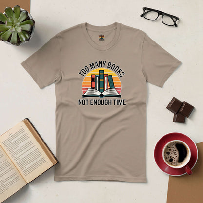 Beige tee with "Too Many Books, Not Enough Time" text, open book graphic, surrounded by coffee, glasses, chocolates, and an open book.