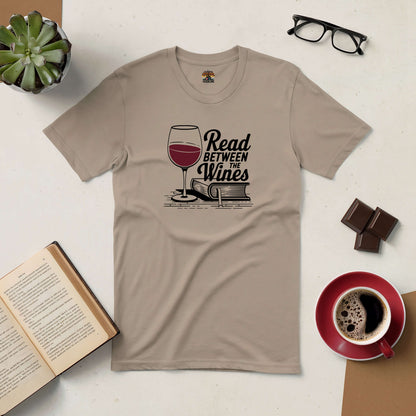 "Read Between the Wines Tee with wine and book graphic, perfect for book and wine lovers, surrounded by coffee, book, and glasses"