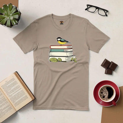 Beige tee with bird on stacked books, alongside coffee and glasses, ideal for book lovers and nature enthusiasts.