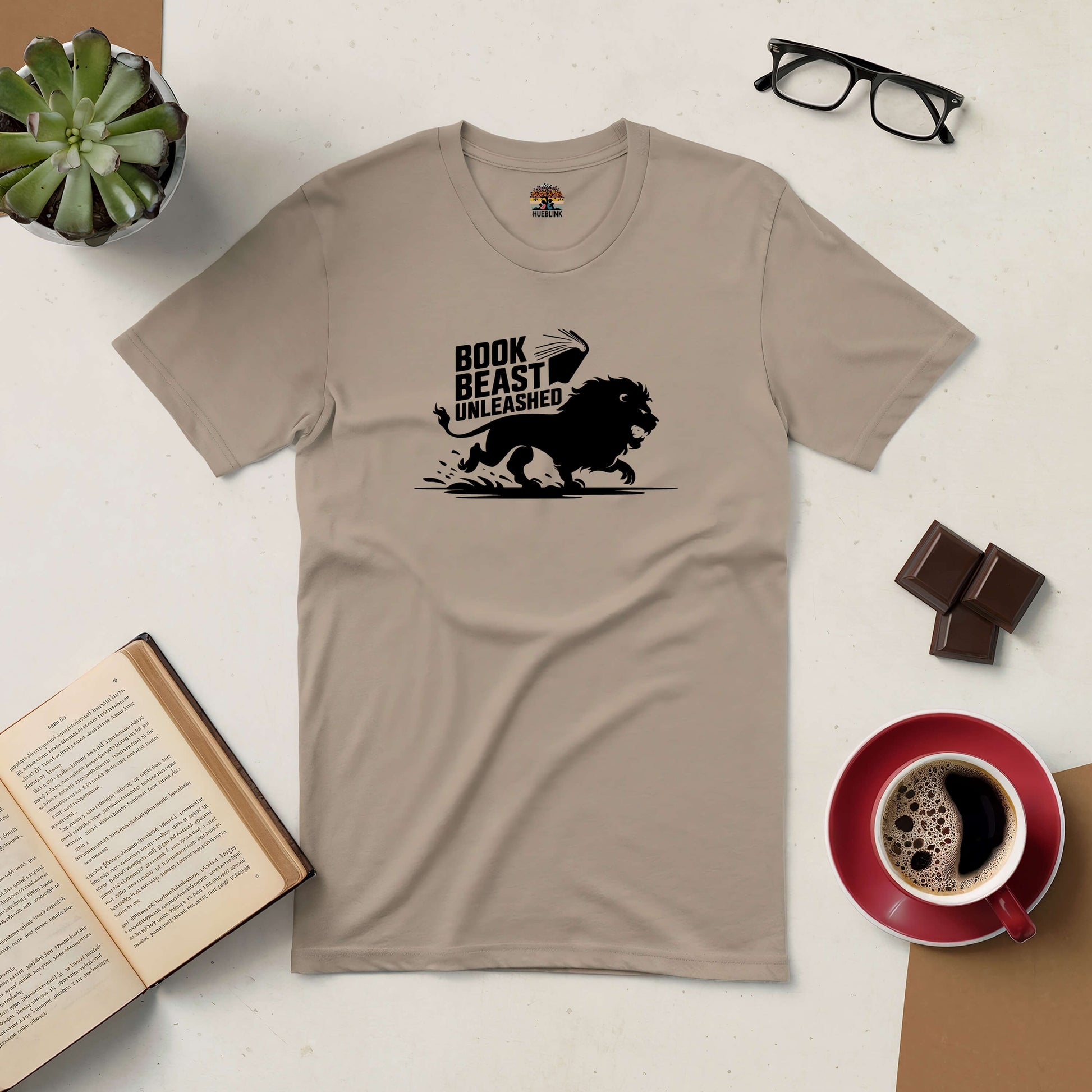 Book Beast Unleashed tee with lion design for avid readers, includes open book, coffee, and glasses on a table.