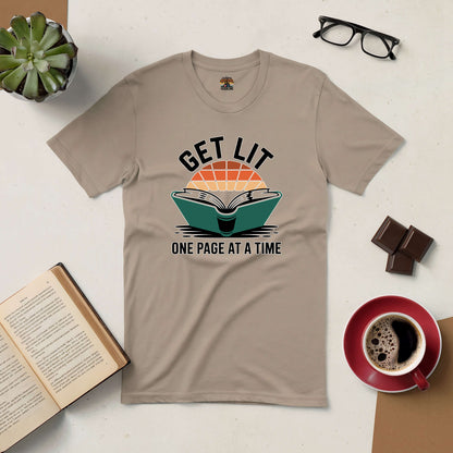 Tan "Get Lit: One Page At A Time" tee for book lovers placed on a flat surface with a book, coffee, glasses, and plant.