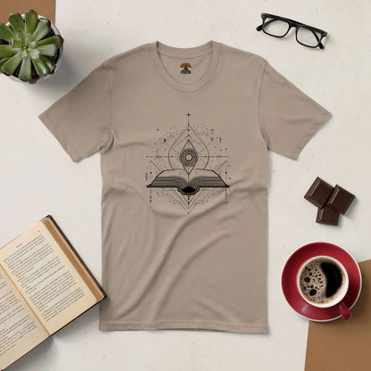 "Portal to Knowledge Tee with mystical book design, surrounded by a coffee cup, chocolate, open book, glasses, and a plant"