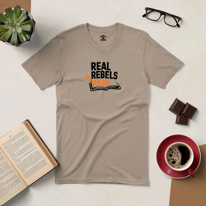 Real Rebels Read tee on a table with an open book, coffee, chocolate, glasses, and a plant.