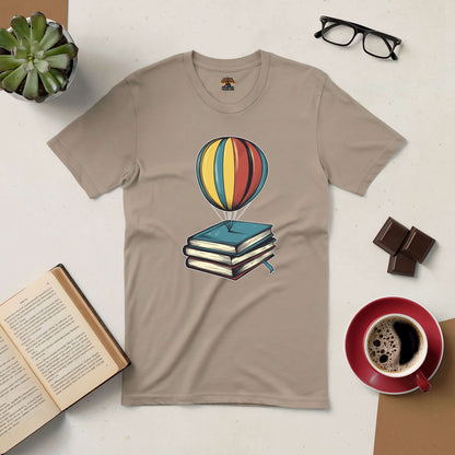 Passport to Dreamland tee with hot air balloon and books design, surrounded by coffee, open book, glasses, and chocolate.