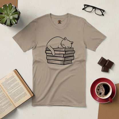 Beige t-shirt featuring a cat napping on a stack of books, surrounded by coffee, chocolates, glasses, and an open book.