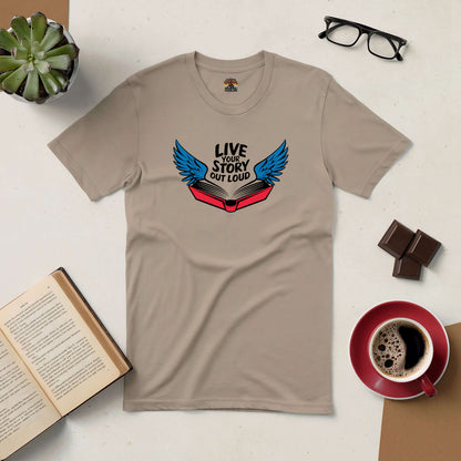 Beige tee with open book and wings design, "Live Your Story Out Loud," surrounded by coffee, glasses, and an open book.