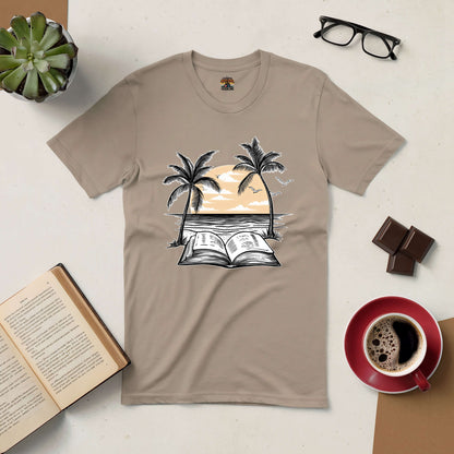 Beachside Bibliophile Tee with palm trees, open book, and sunset print, surrounded by coffee, glasses, chocolate, and a potted plant.