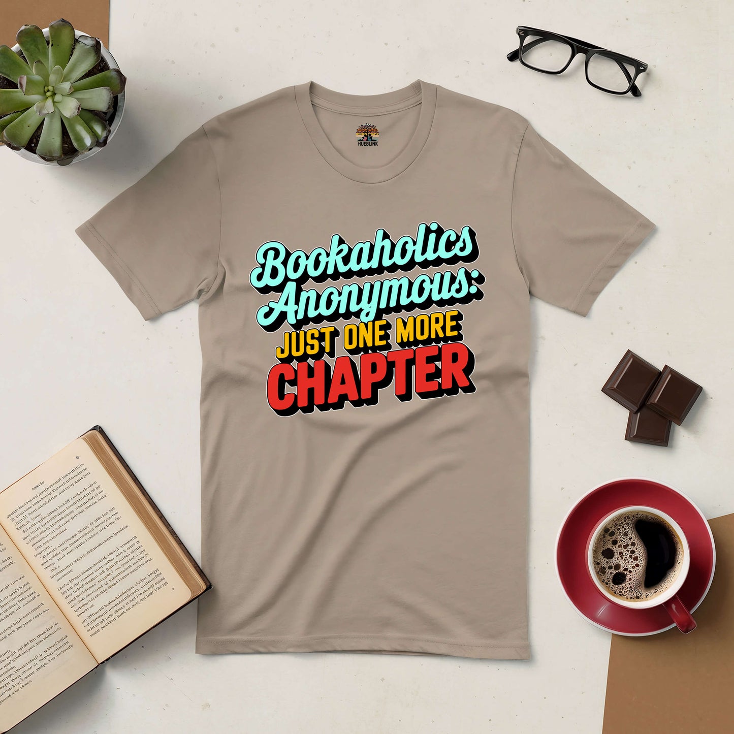 Bookaholics Anonymous Tee with "Just One More Chapter" design, surrounded by books, glasses, coffee, and chocolate.