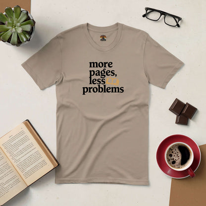 Beige "More Pages, Less Problems" tee for book lovers, surrounded by a book, coffee, glasses, chocolate, and a succulent on a table.