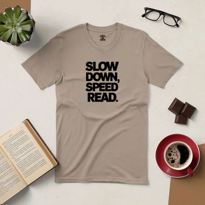 Beige t-shirt with "Slow Down, Speed Read" text, surrounded by coffee, glasses, chocolate, book, and a small plant on a table.