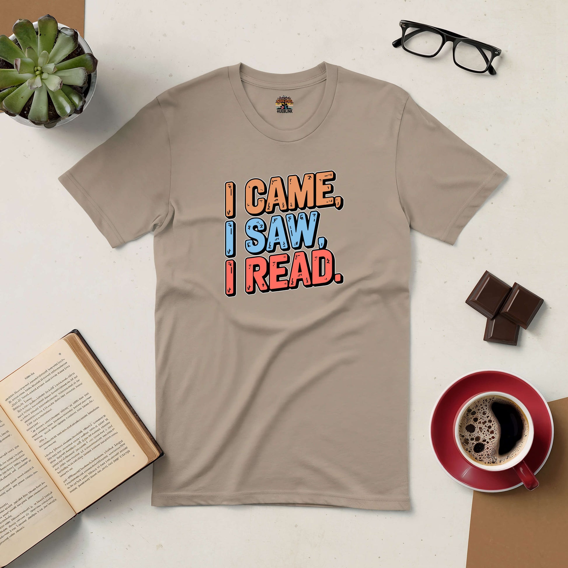 Beige t-shirt with "I Came, I Saw, I Read" text for book lovers, surrounded by coffee, glasses, chocolate, and an open book.