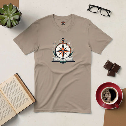 Beige T-shirt with compass and open book design. Coffee, glasses, and succulent in the background.